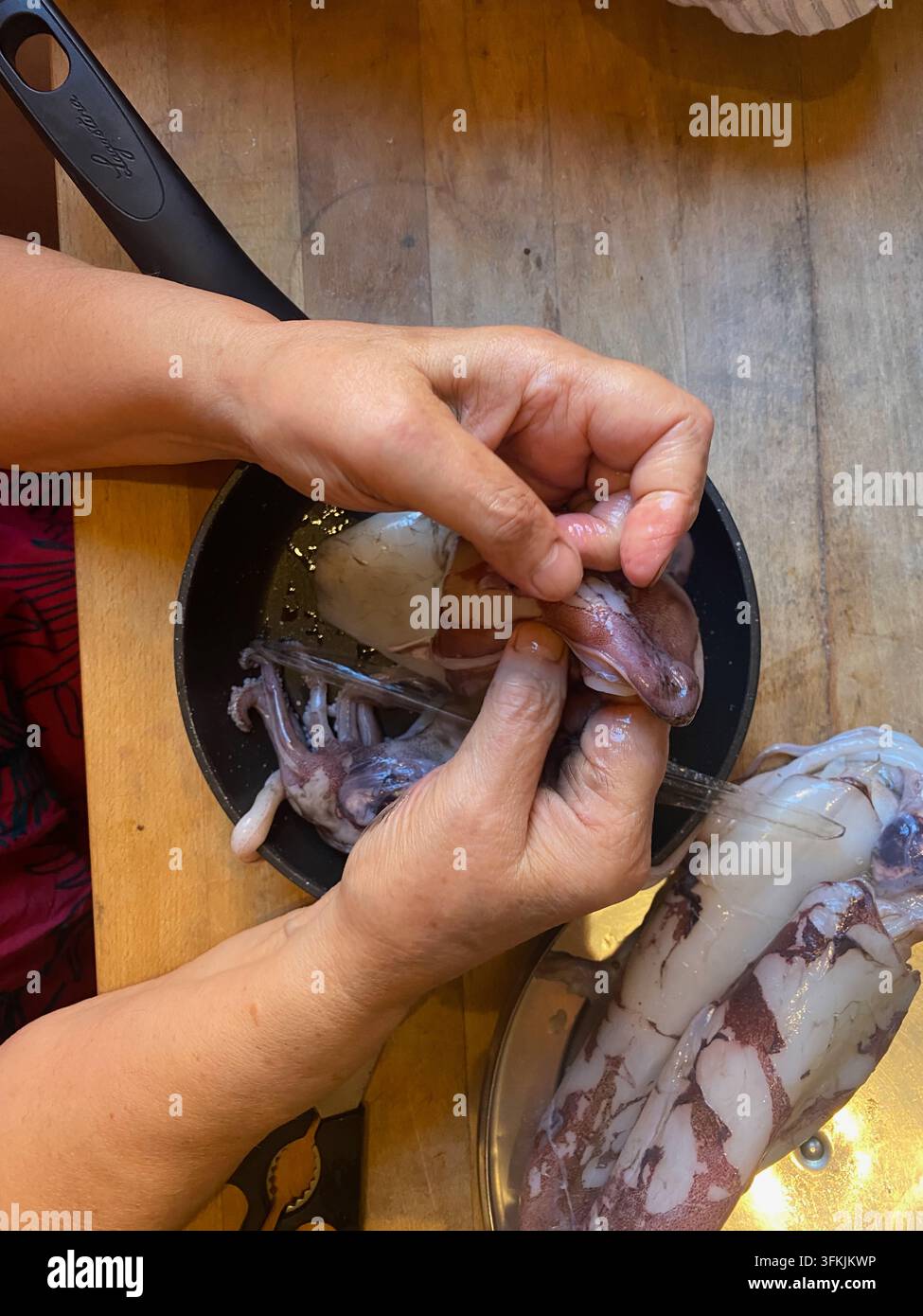 Mani che puliscono con cura il polpo crudo, rimuovendo le parti interne e i tentacoli in un contesto di cucina, preparando frutti di mare freschi per un pasto sano e saporito Foto Stock