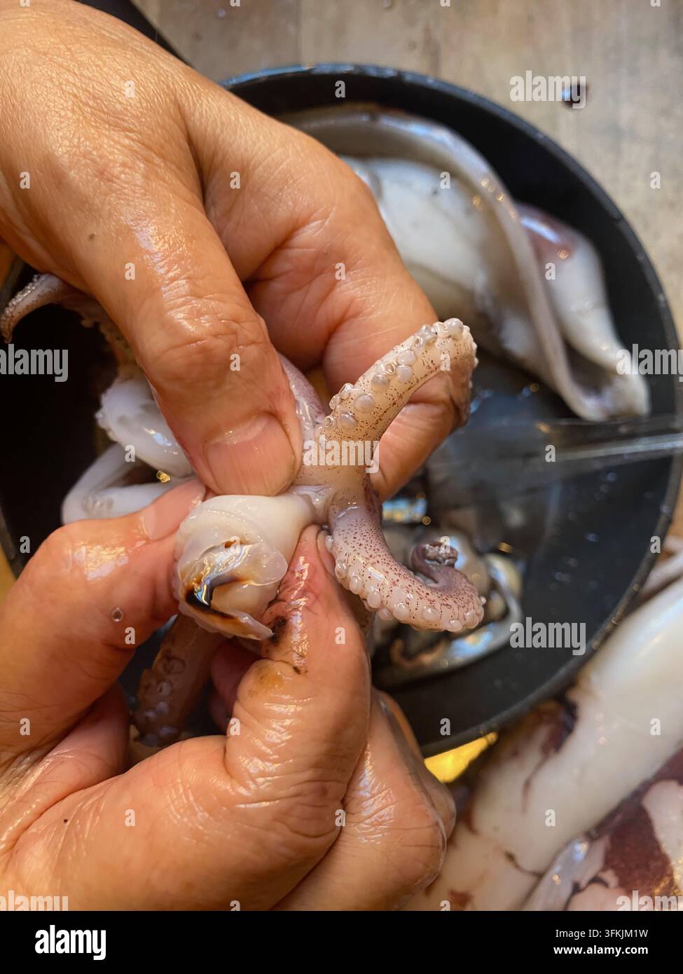 Mani che puliscono calamari freschi per la cottura, rimuovendo la sacca dell'inchiostro e il becco dai tentacoli di cefalopodi crudi in una cucina, primo piano della preparazione alimentare per un gourmet Foto Stock