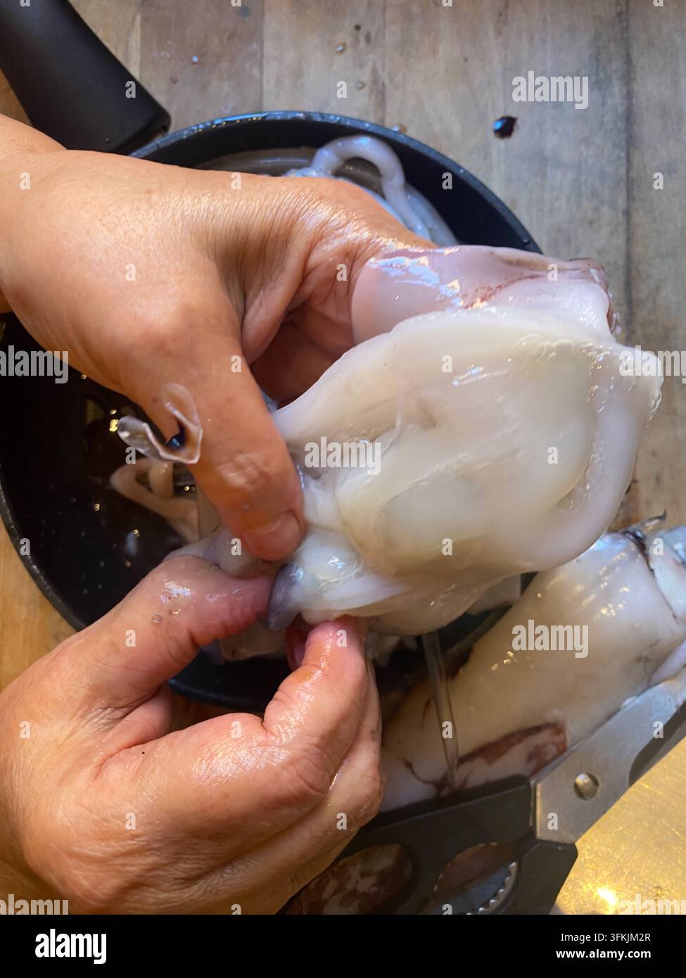 Mani che puliscono il calamaro crudo, rimuovendo la sacca dell'inchiostro e le parti interne in una ripresa dall'alto della cucina, preparando frutti di mare freschi per calamari e altri piatti gourmet Foto Stock
