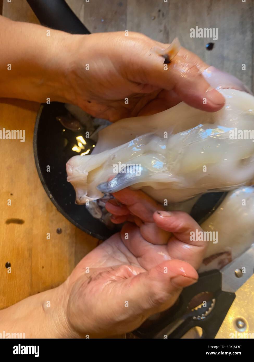 Mani che puliscono il calamaro crudo, rimuovendo la sacca dell'inchiostro e le parti interne in una ripresa dall'alto della cucina, preparando frutti di mare freschi per calamari e altri piatti gourmet Foto Stock