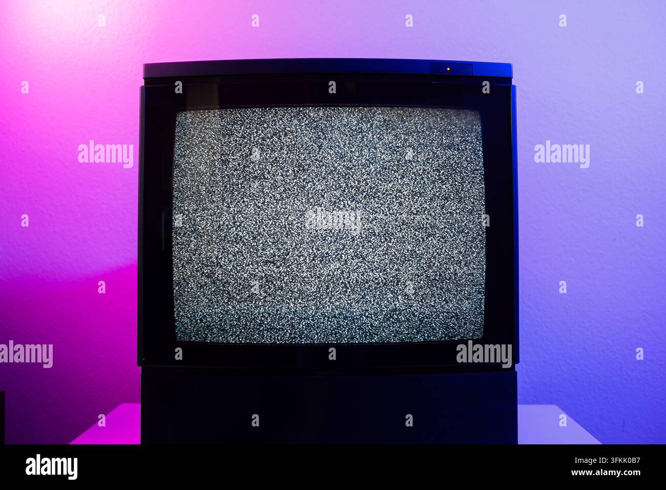 Inquadratura centrata su un televisore CRT vintage che mostra uno schermo statico con rumore bianco su uno sfondo murale colorato al neon viola e rosa Foto Stock
