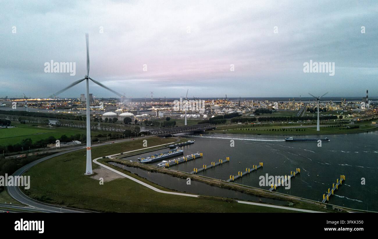 Vista aerea di un'area portuale industriale al crepuscolo, che mostra una turbina eolica, chiatte e un grande complesso di raffineria Foto Stock