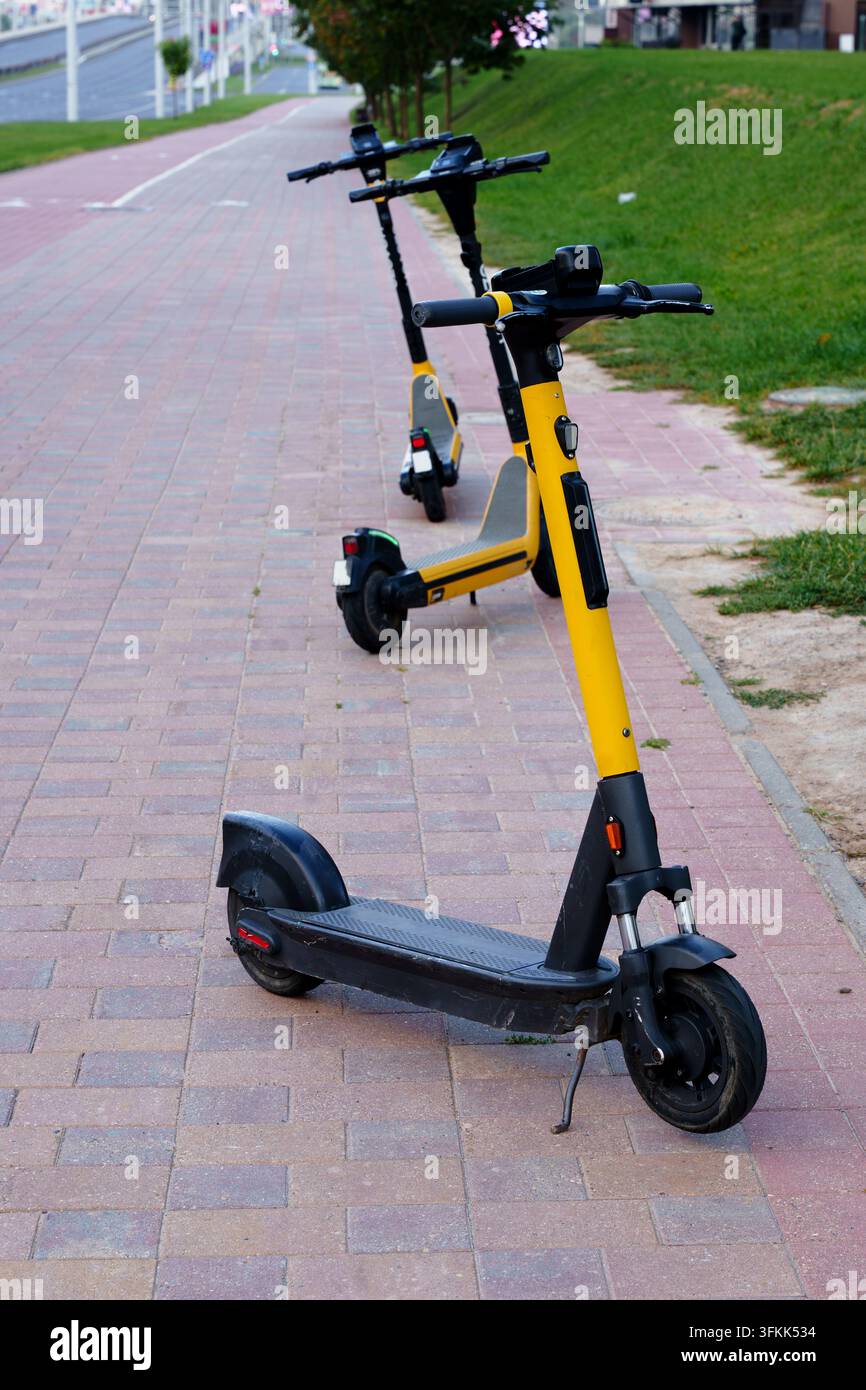 Scooter elettrici gialli parcheggiati su un marciapiede cittadino. Concetto di micro-mobilità urbana e trasporto alternativo ecologico Foto Stock