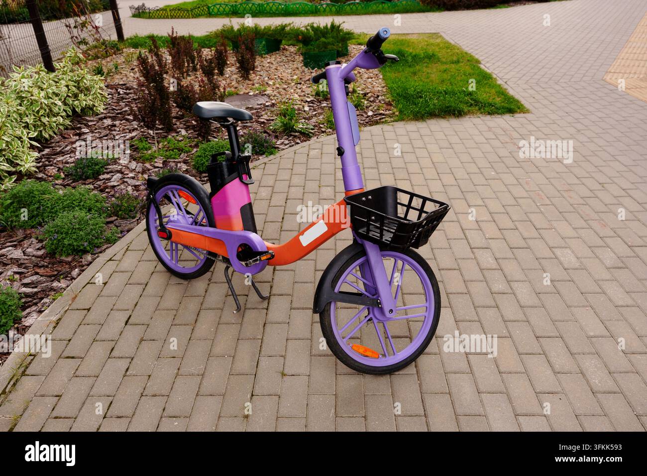 Bicicletta elettrica moderna viola e arancione parcheggiata sul marciapiede cittadino Foto Stock