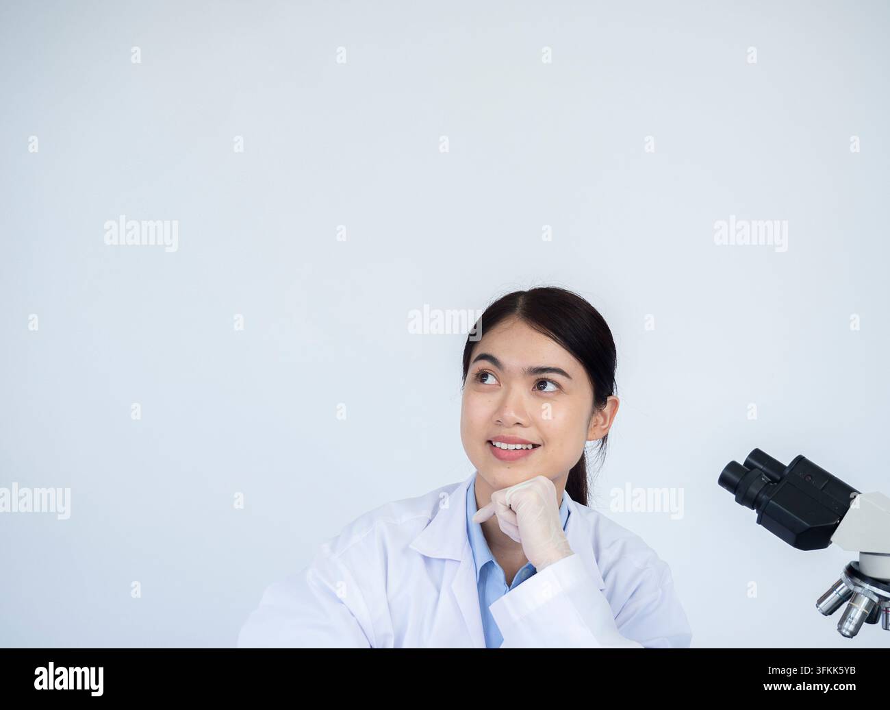 Ritratto di uno scienziato di laboratorio diagnostico felice e soddisfatto davanti allo spazio per la copia e al camice bianco, seduto in un laboratorio clinico e sorridendo mentre guarda verso l'alto Foto Stock