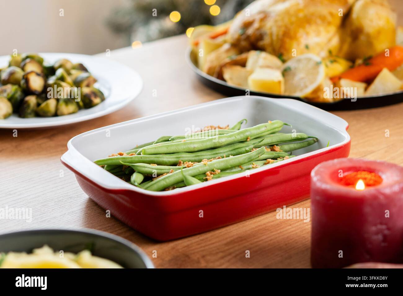 Fagiolini con cipolle fritte croccanti serviti in una pirofila rossa, circondati da tacchino arrosto, cavoletti di Bruxelles e verdure su un festoso Foto Stock
