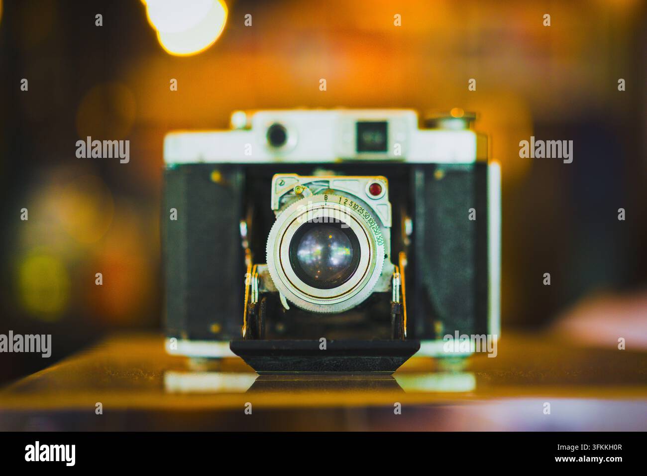 Fotografia vintage e concetto di macchina fotografica retrò, macchina fotografica pieghevole antica a soffietto con obiettivo cromato appoggiata su tavolo con bokeh caldo, simboleggia l'analogico Foto Stock