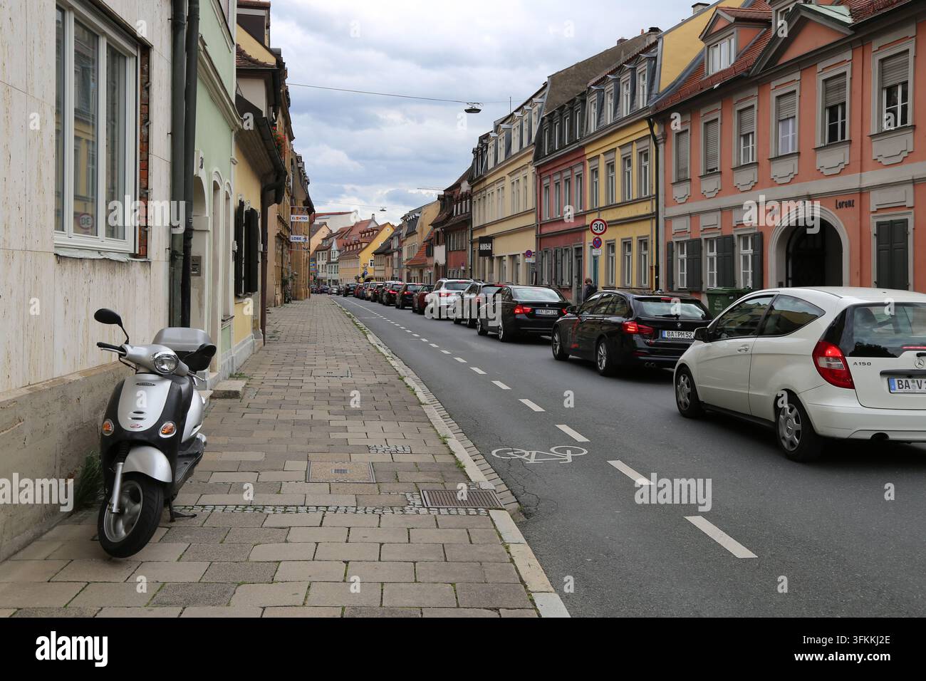 Vista di strada di una città storica tedesca con edifici tradizionali colorati, uno scooter parcheggiato sul marciapiede e auto a Bamberg, Germania Foto Stock