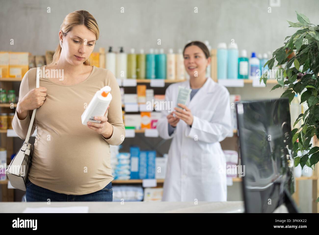 Donna incinta sceglie una crema per il rash da pannolino in farmacia, esamina la confezione. Rimedio per il rash da pannolino, crema protettiva per il pannolino. Farmacista sullo sfondo offre s Foto Stock