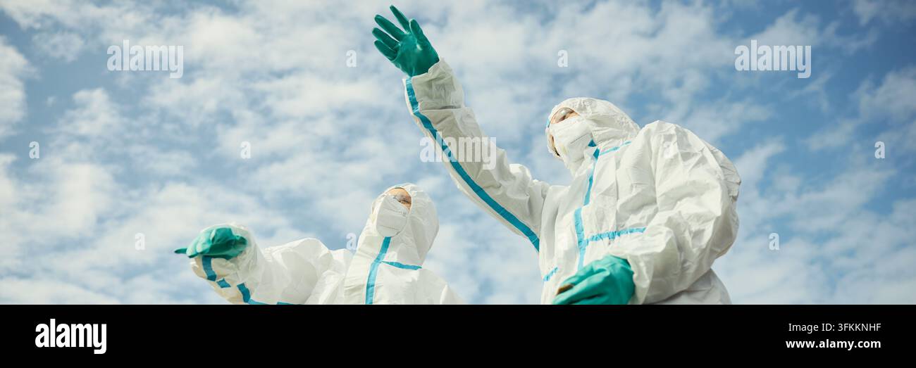 Testa di scienziati in tute protettive che puntano verso il cielo all'aperto Foto Stock
