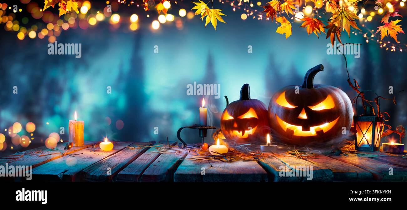 Zucchine di Halloween - Jack O’ Lantern su tavolo di legno in foresta sfocata blu di notte con luci bokeh astratte Foto Stock