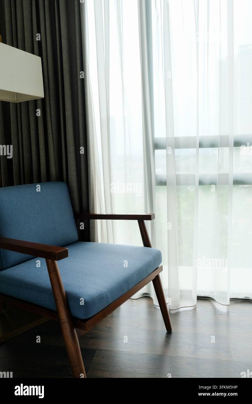 Sedia moderna con accento blu e struttura in legno nell'angolo di una camera d'albergo Foto Stock