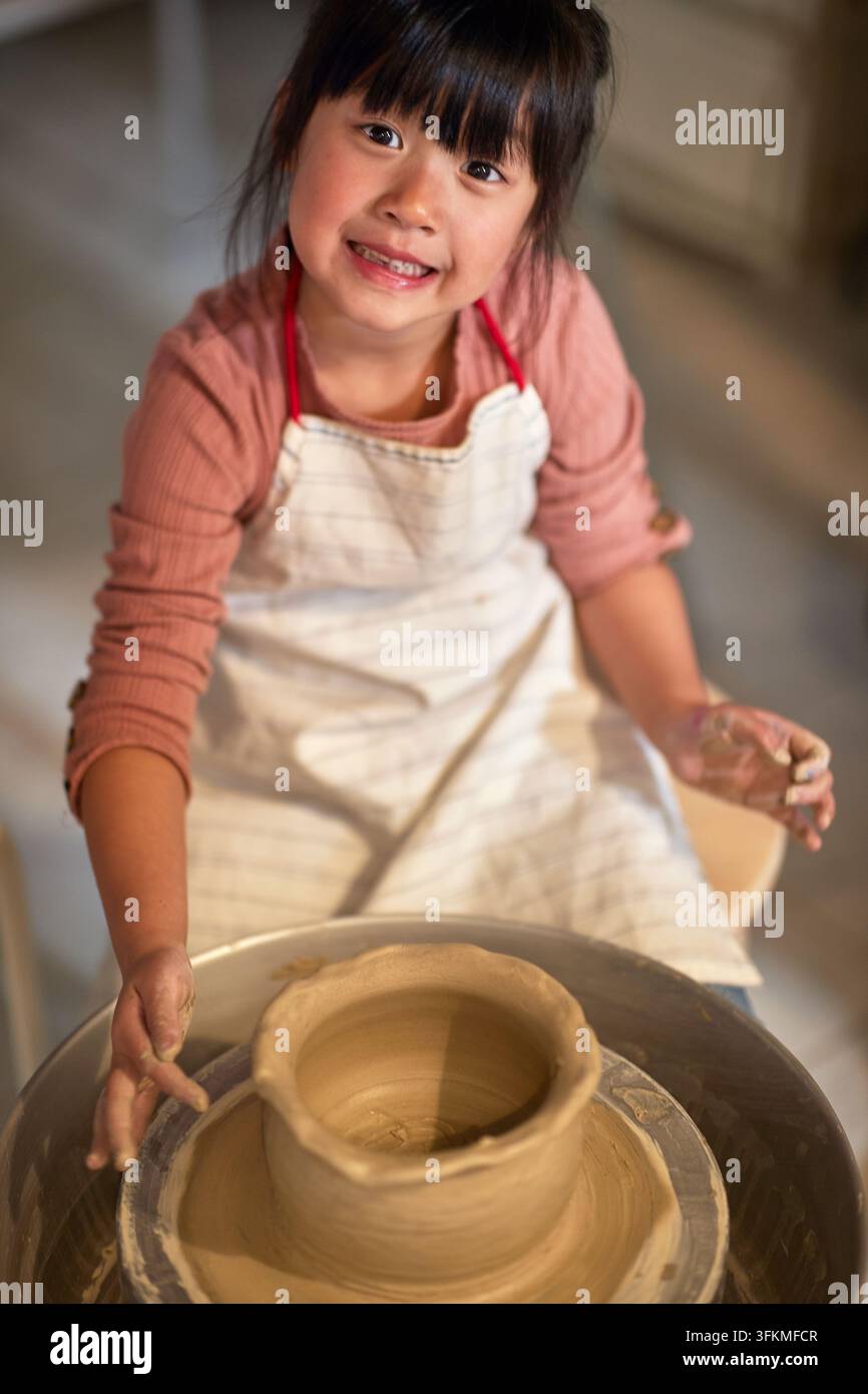 ragazza cinese felice che crea una ciotola di argilla su una ruota rotante nella scuola di ceramica. Concetto creativo, hobby, workshop Foto Stock