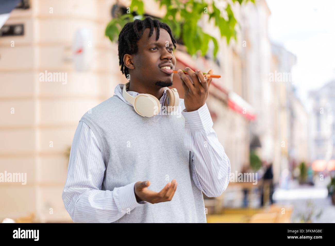 Giovane uomo afroamericano che parla al telefono mentre cammina per una strada cittadina, spiegando tramite vivavoce. Turista nero che gesticola all'aperto durante una chiamata vocale condividendo indicazioni o consigli di viaggio in città Foto Stock