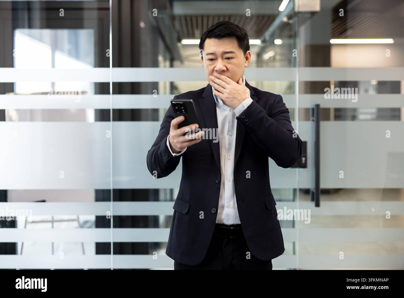 Cattive notizie e crisi aziendale, uomo d'affari preoccupato che guarda lo smartphone con espressione scioccata in ufficio. Uomo professionista che legge un messaggio negativo sullo schermo del telefono cellulare mentre prova una profonda preoccupazione. Foto Stock
