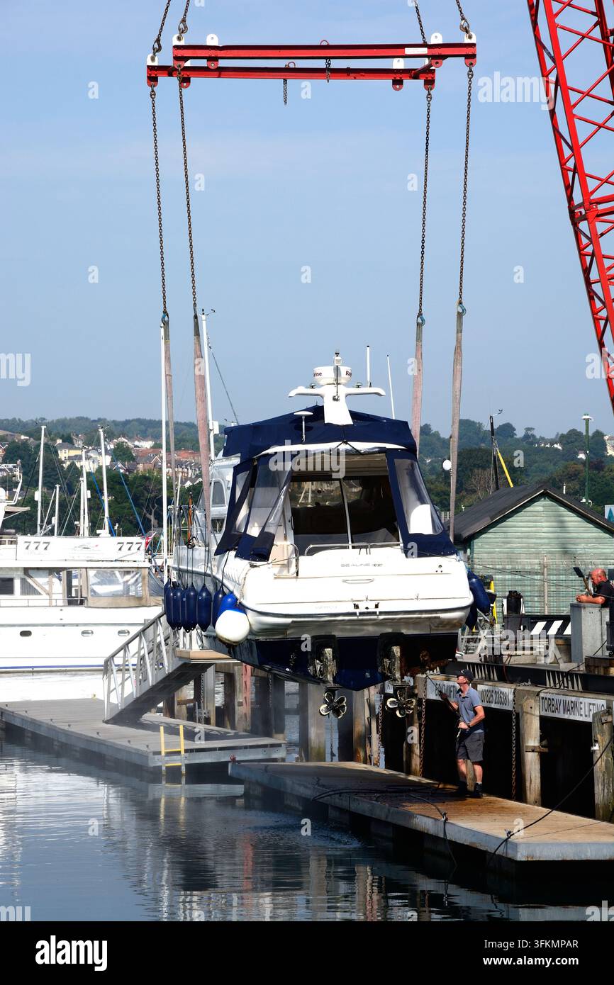 Barca a motore sollevata fuori dalla marina da una gru per la pulizia, Torquay, Devon, Regno Unito, Europa. Foto Stock