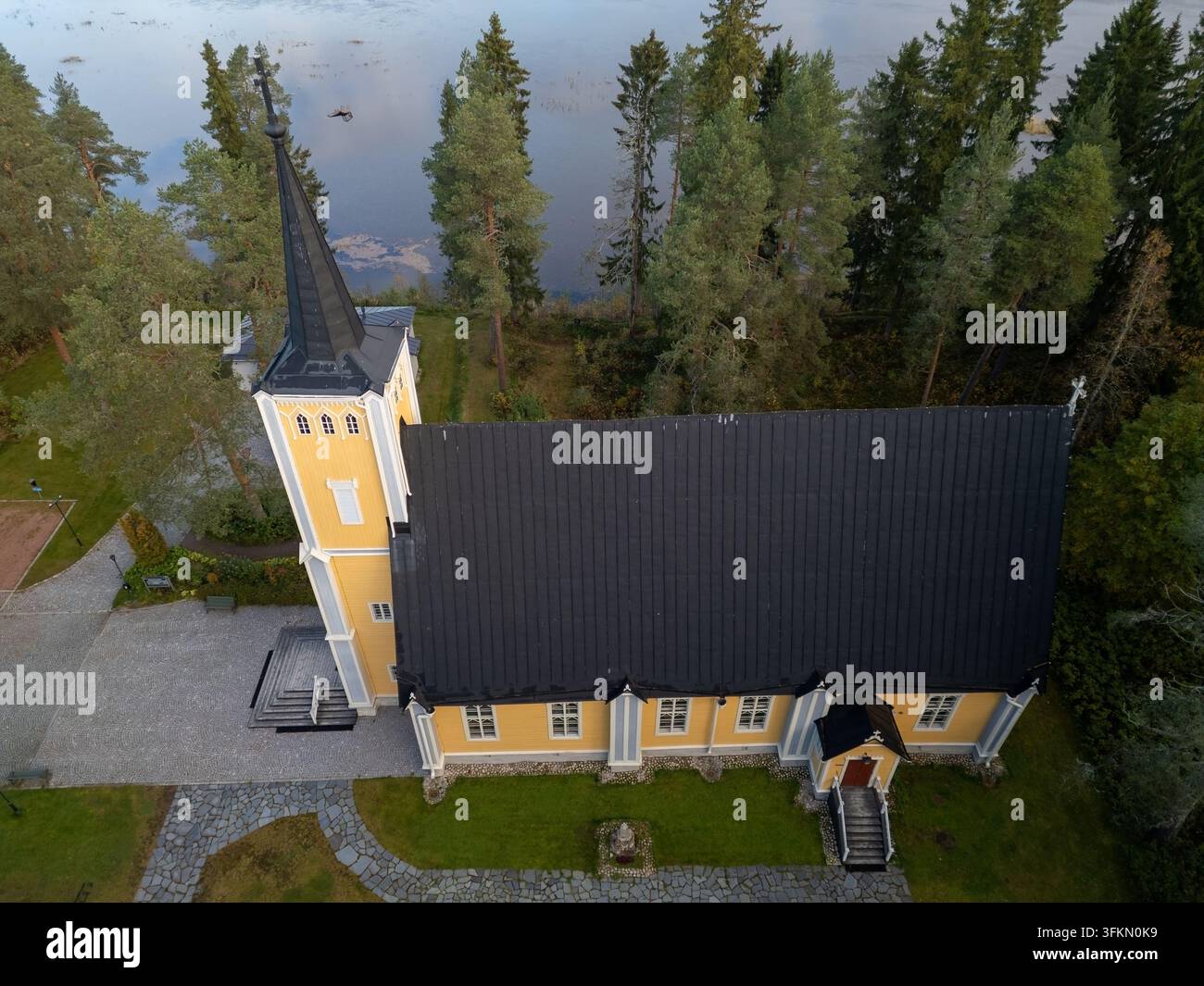 Vista aerea della chiesa storica di Muhos con le sue pareti in legno giallo e il tetto scuro, circondata da pini e prati verdi a Muhos, Ostrobotnia del Nord Foto Stock