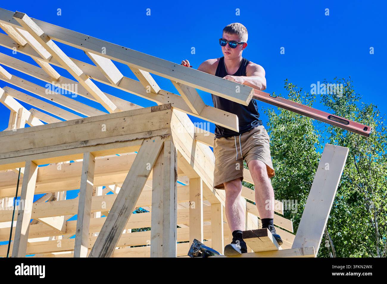 Per marcare le travi, un operaio edile utilizza un'impalcatura lavorando in altezza durante la costruzione di una casa a telaio. Foto Stock