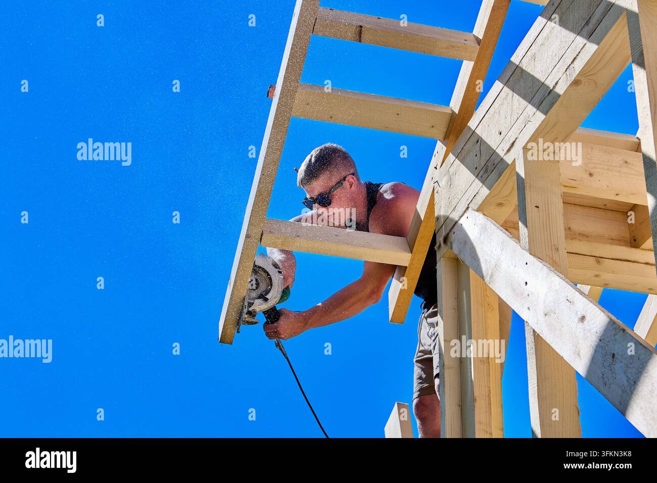 Sega circolare taglia travi del tetto mentre un operaio edile taglia un elemento di legno durante l'assemblaggio di una struttura a telaio di legno in cantiere. Foto Stock