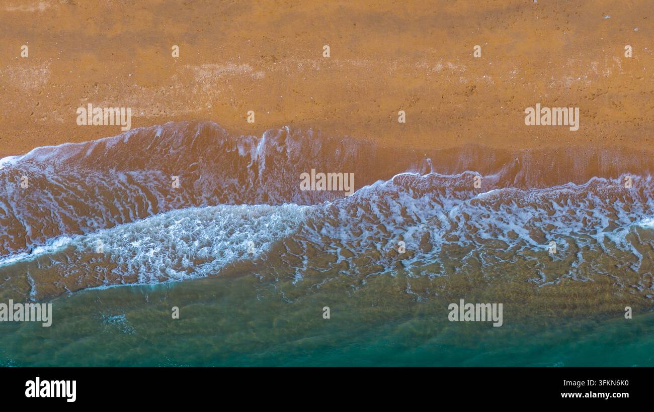 Vista aerea della costa con onde gentili che si infrangono sulla sabbia dorata e sull'acqua turchese a West Bay, Inghilterra, Regno Unito. Foto Stock