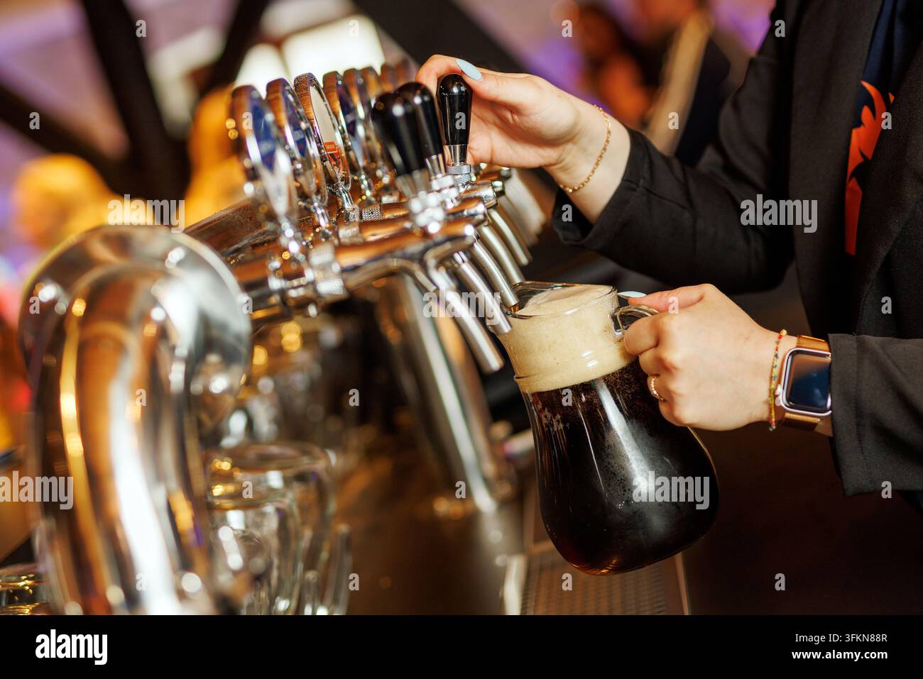 Prima piano di un barista che usa una spina per versare una birra artigianale scura e fresca con una spessa schiuma in una caraffa di vetro. Scatto dinamico che mostra l'ospitalità Foto Stock