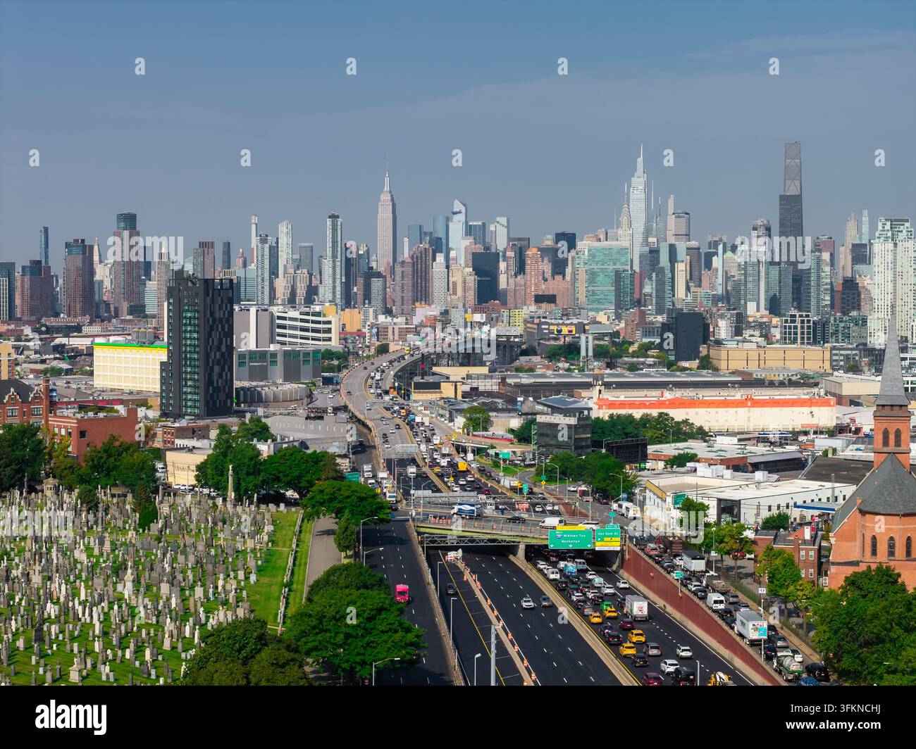 Vista aerea che cattura il traffico lungo la Long Island Expressway a Queens, accanto al Calvary Cemetery, di fronte all'iconica skyline di Midtown Manhattan i Foto Stock