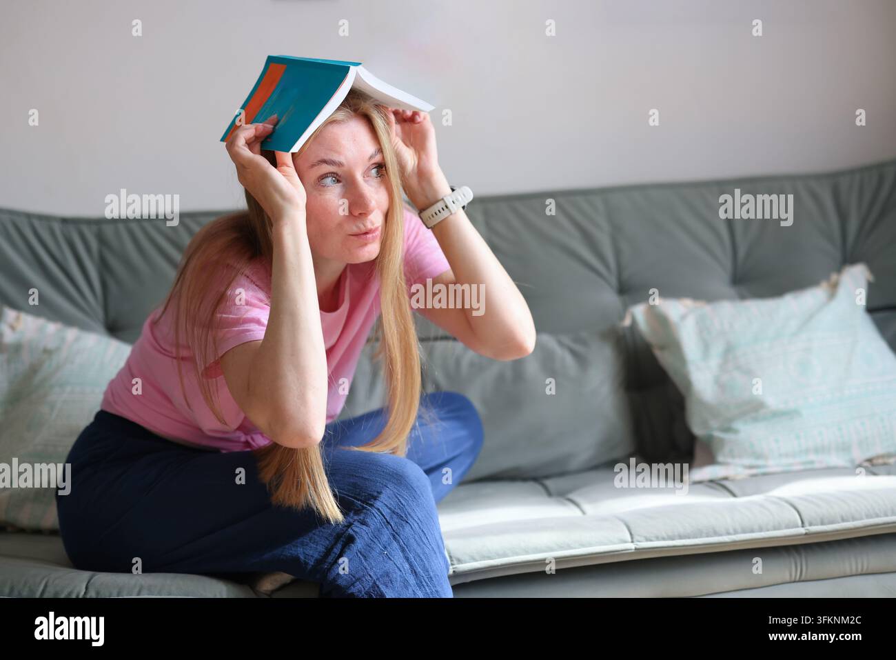 Lettrice che abbraccia libri colorati su un divano, illustrando l'amore per la letteratura, la conoscenza e il tempo libero accogliente in casa. Foto Stock