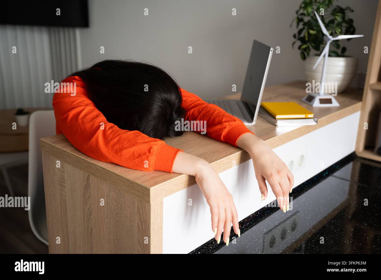 Donna che riposa la testa su una scrivania dell'ufficio domestico accanto a un laptop e materiali di studio. Consapevolezza del burnout da lavoro remoto e sovraccarico di studio online. Foto Stock