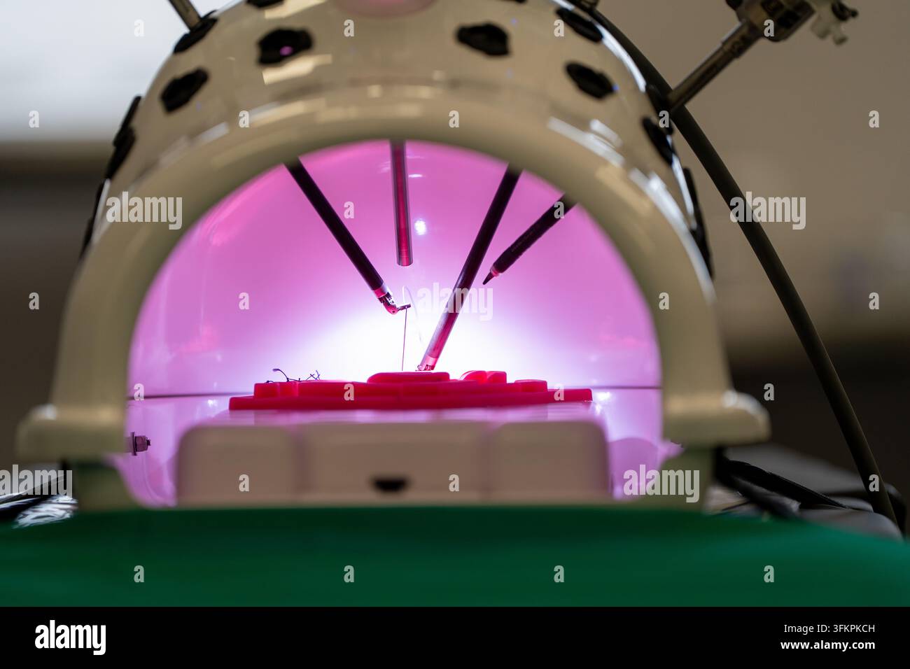 Bracci di strumenti robotici chirurgici che eseguono una procedura simulata sotto luce rosa, concetto di formazione in tecnologia medica. Foto Stock