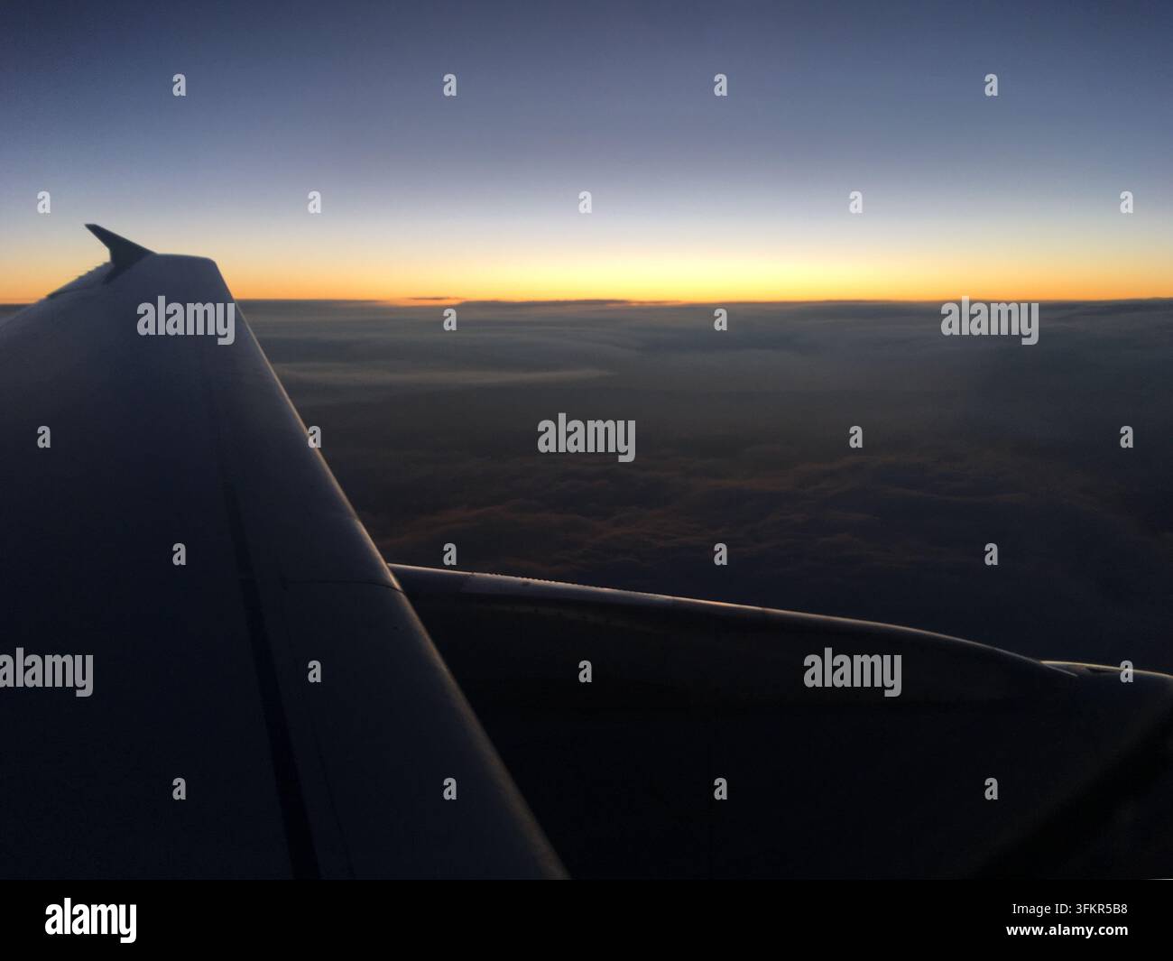 Vista da un finestrino dell'aereo che mostra l'ala e un orizzonte sereno al tramonto. L'immagine cattura la sfumatura dei colori nel cielo, che si trasforma Foto Stock