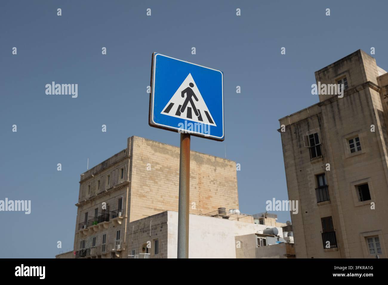 Un cartello stradale blu con un triangolo e una grafica di un omino che attraversa la strada situato a La Valletta, Malta. Foto Stock