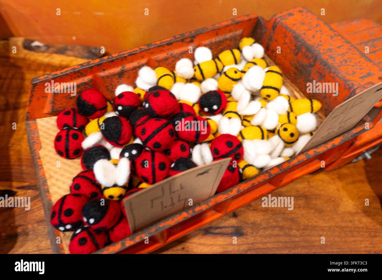 Giocattoli in feltro colorati fatti a mano disposti all'interno di una cassa di legno consumata: coccinelle rosse e nere con api a strisce gialle, texture morbida in tessuto per scaffali per bambini Foto Stock