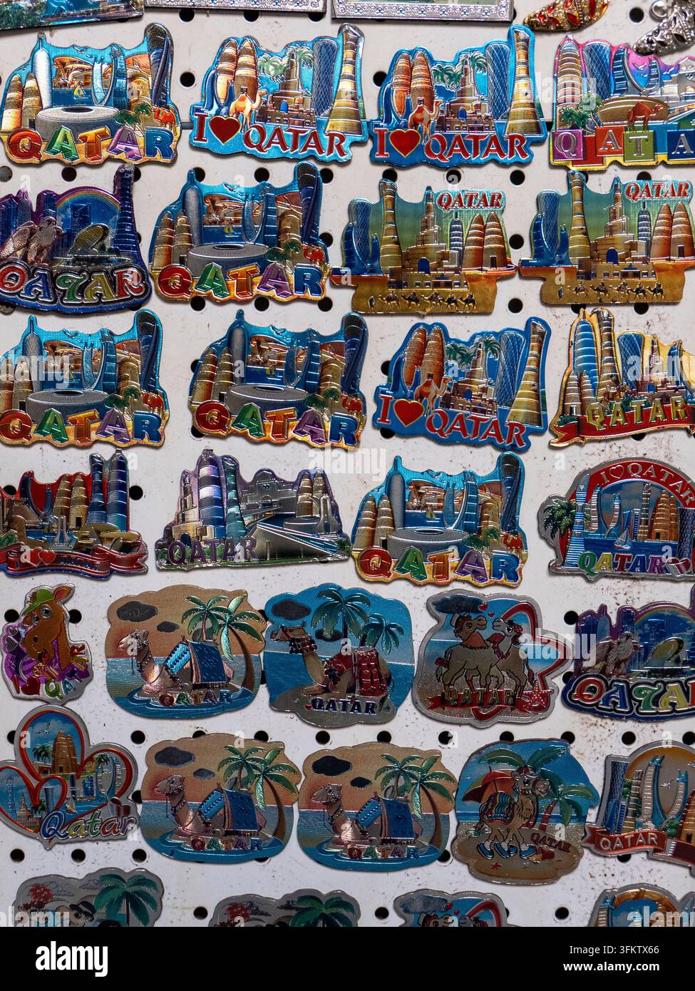 Collezione di magneti colorati da frigorifero con souvenir raffiguranti vari monumenti del Qatar e disegni dello skyline di Doha esposti su una bacheca. Foto Stock
