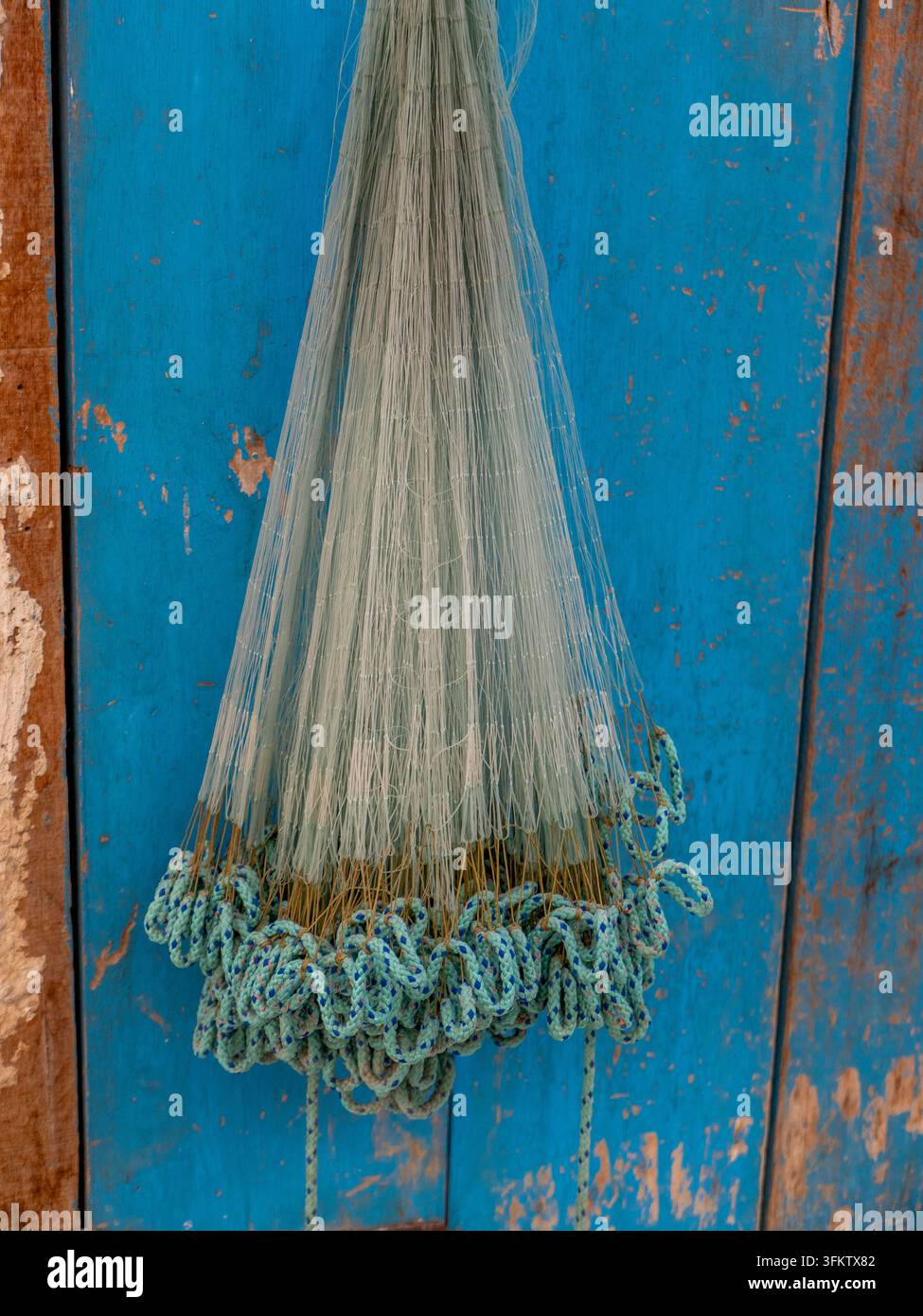 Rete da pesca tradizionale in nylon con bordi di corda appesantiti appesa davanti a una porta di legno blu scolorita nel Souq Waqif di Doha. Foto Stock
