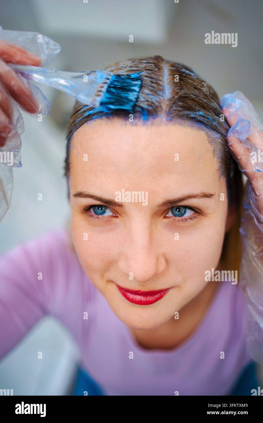 Donna che applica tinture blu per capelli a casa Foto Stock