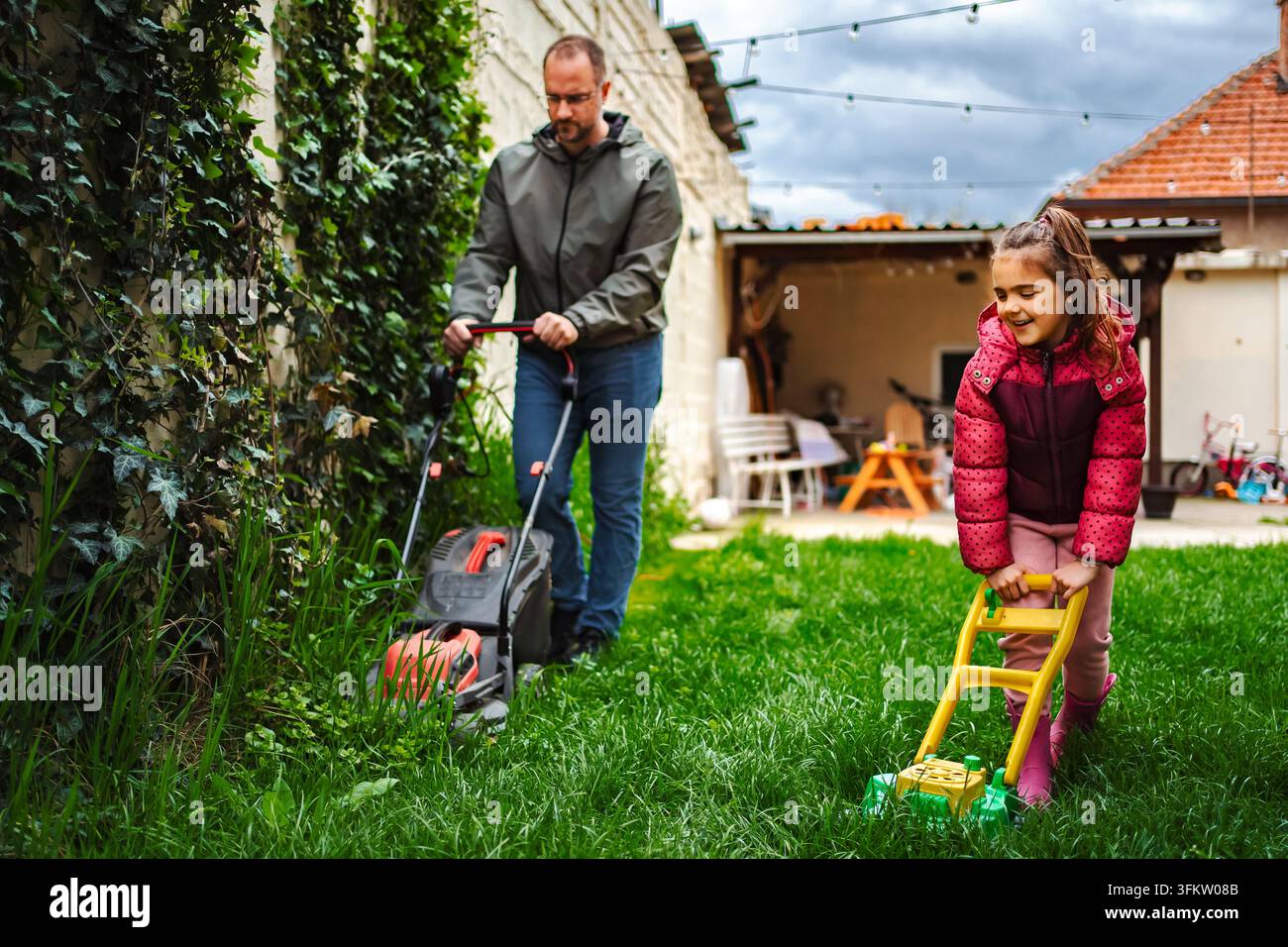 Padre e figlia che tagliano l'erba insieme nel cortile sul retro Foto Stock