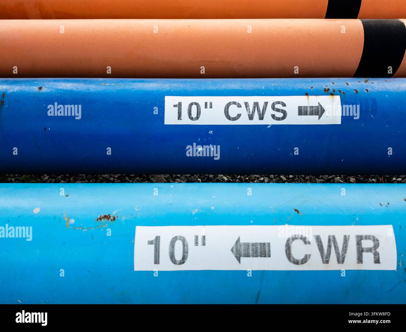 Primo piano delle etichette di identificazione dei tubi che segnalano i tubi CWS (Fornitura di Acqua di Raffreddamento) e CWR (Ritorno di Acqua di Raffreddamento) in un impianto industriale, mostra stan Foto Stock