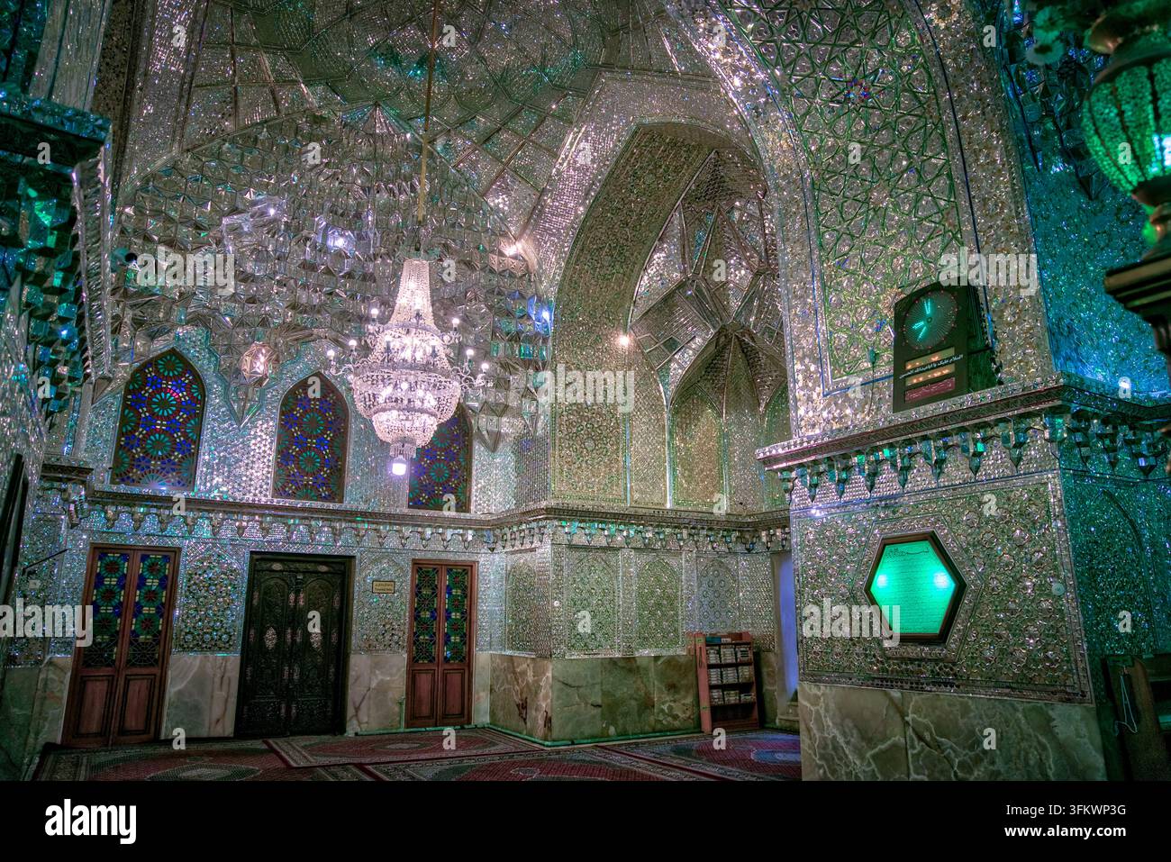Shiraz, Iran - 4 maggio 2019: sala del santuario di Shah Cheragh, con pareti e volte completamente ricoperte di mosaico a specchio, illuminata da un lampadario di cristallo e una lampada verde Foto Stock