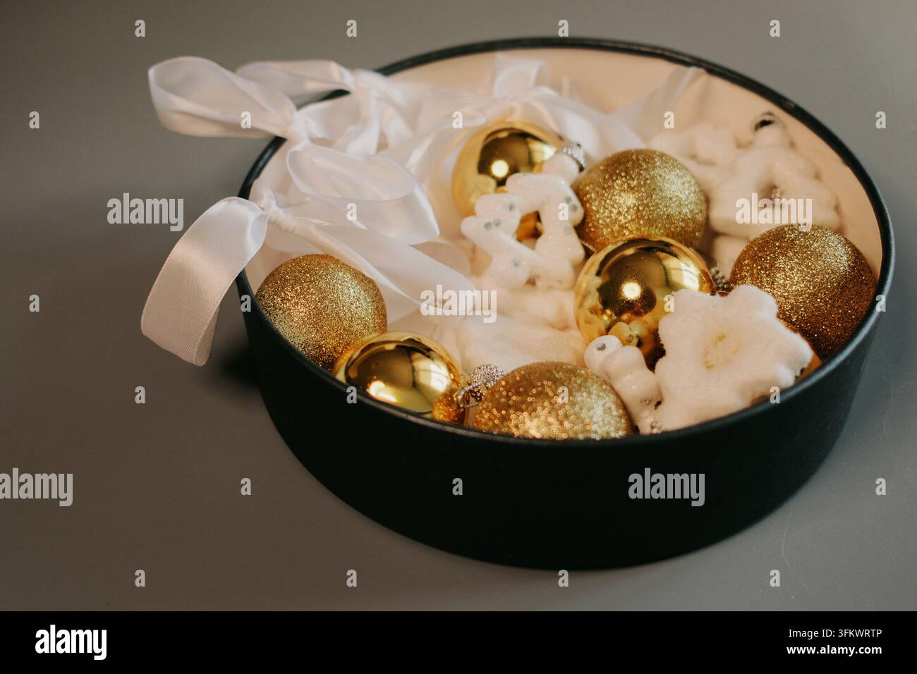 Eleganti ornamenti natalizi dorati e decorazioni a forma di fiocco di neve bianchi disposti in una ciotola scura, che formano un centrotavola sofisticato per le festività invernali Foto Stock