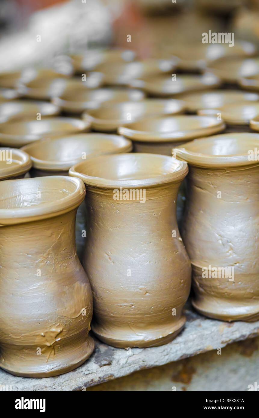 File uniformi di vasi di argilla bagnati allineati per asciugare, catturando la precisione della produzione tradizionale di ceramica Foto Stock