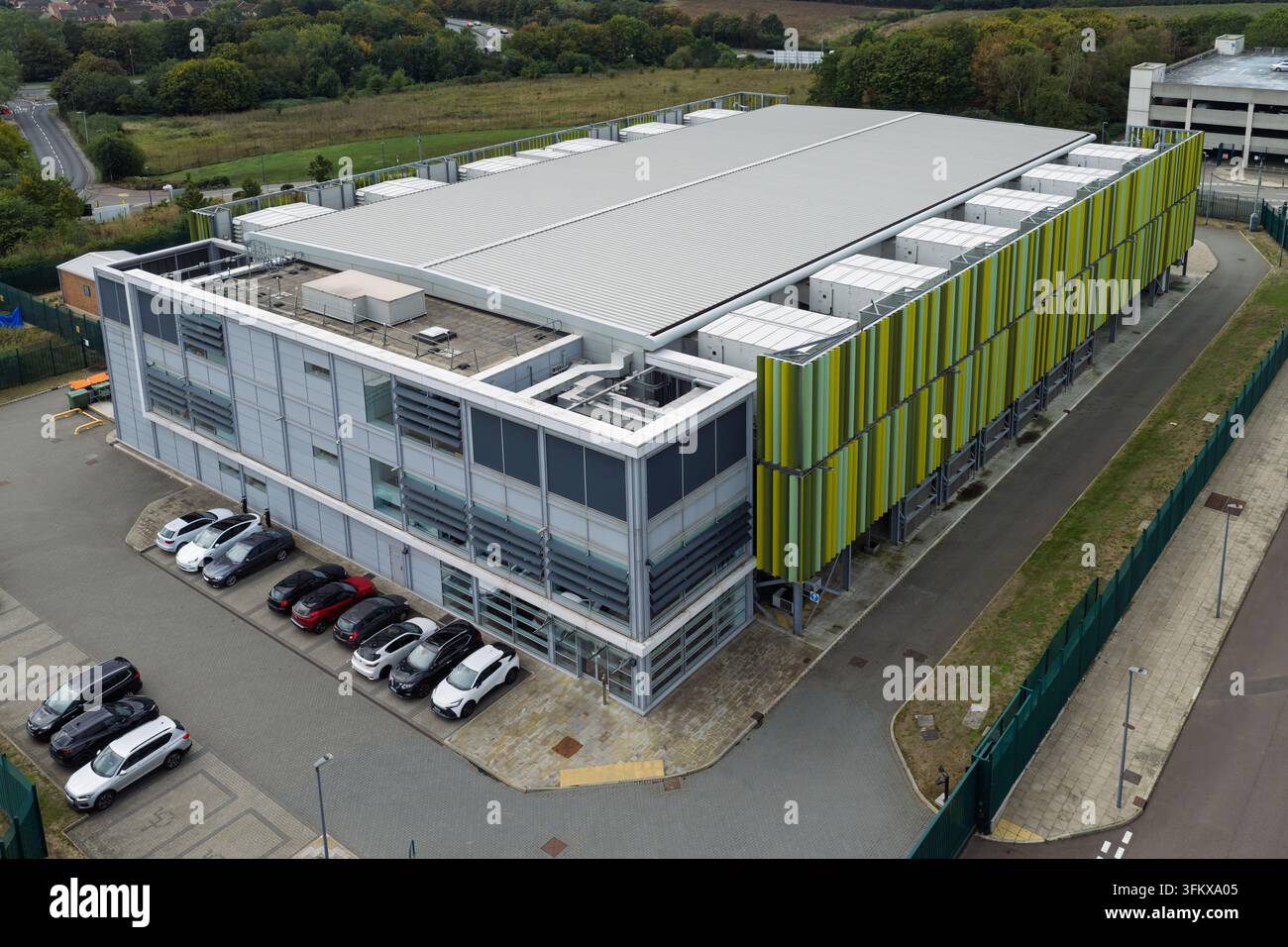 Vista aerea di un moderno edificio di data center con pannelli di facciata verdi e gialli, un tetto piatto con apparecchiature HVAC e un parcheggio con auto Foto Stock