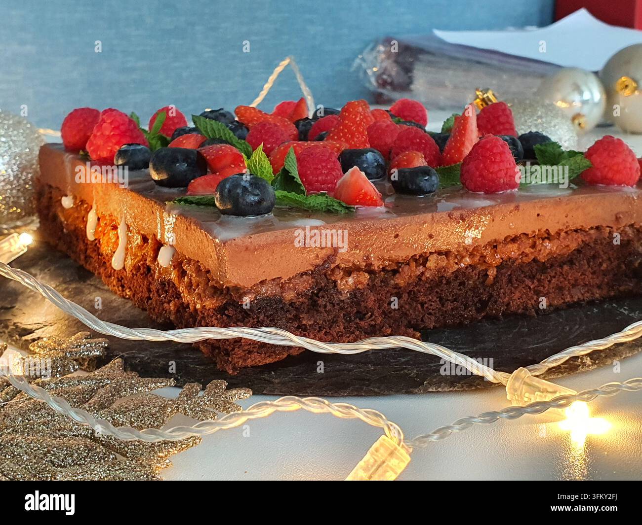 Una torta a strati rettangolare al cioccolato con glassa liscia al cioccolato e gelatina, decorata con lamponi freschi, mirtilli, fette di fragola e Foto Stock