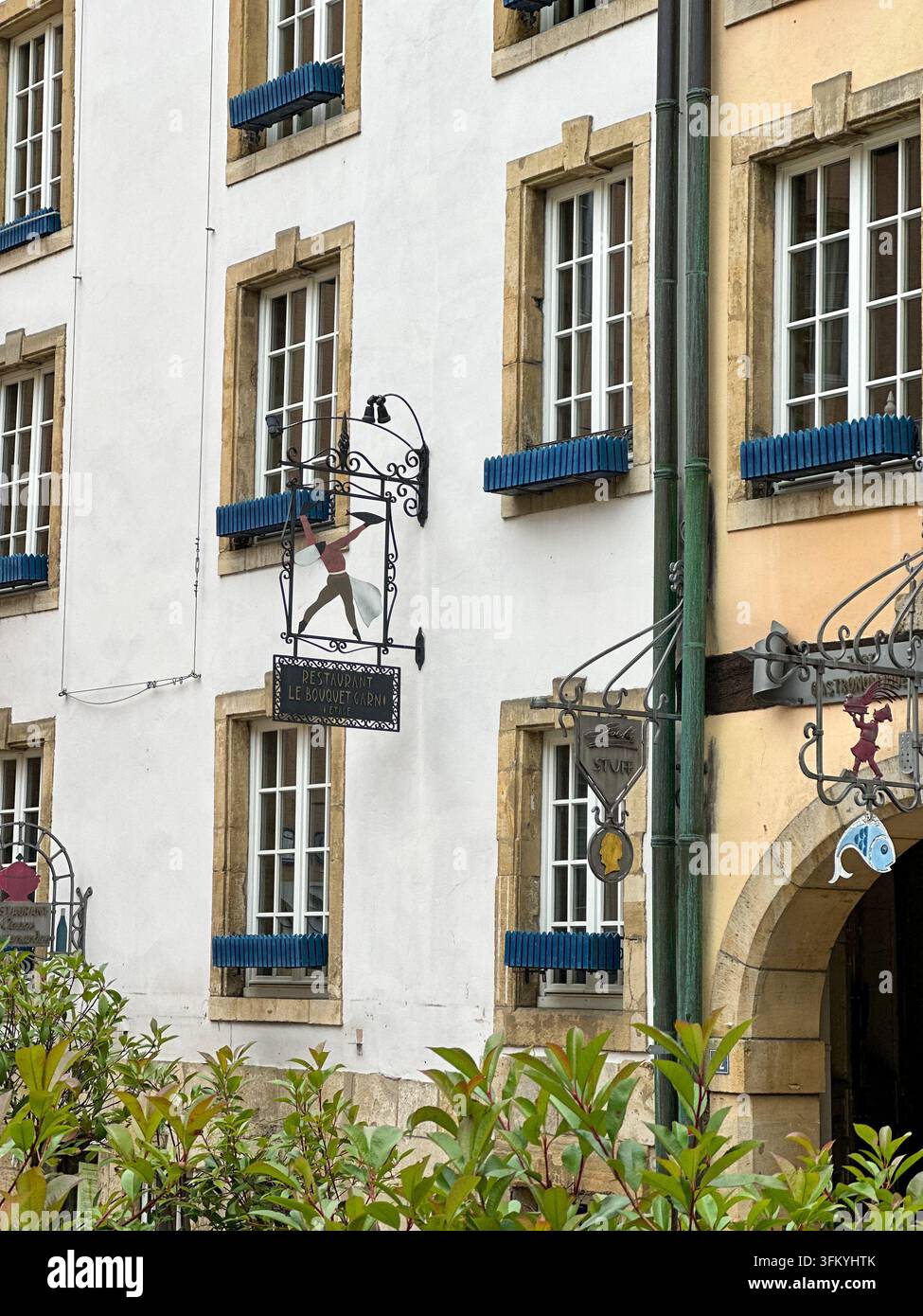 Facciata storica di un edificio bianco con insegne di ristoranti vintage e cassette per fiori blu. Facciata storica di un edificio bianco e giallo con griglia tradizionale - Immagine stock catturata con smartphone