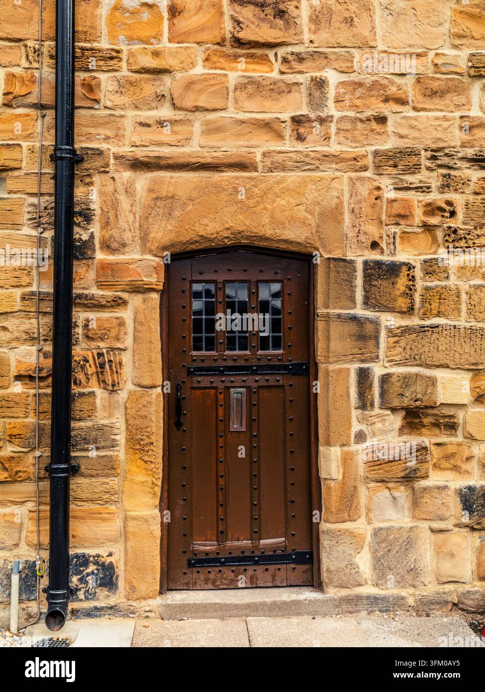 Antica porta di legno chiodata con cerniere di ferro inserita in un muro di arenaria a Durham Foto Stock
