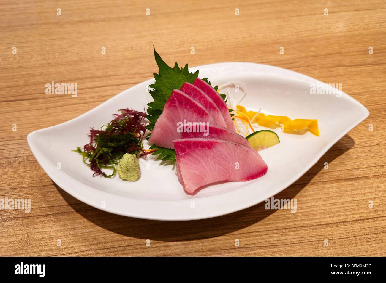 Sashimi di coda gialla affettata fresca servito con alghe shiso, wasabi e guarnizione colorata su un piatto di ceramica bianca in un ristorante giapponese. - Immagine stock catturata con smartphone