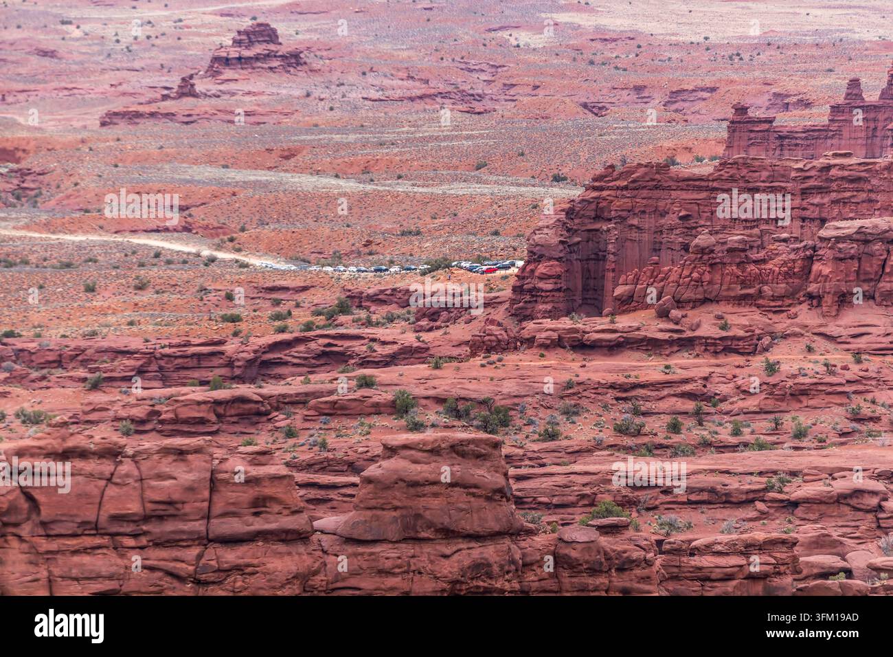 Una vista elevata mostra auto parcheggiate all'inizio del sentiero dei Fisher Towers vicino a Moab, Utah, USA, con torri di arenaria erosi e una strada sterrata attraverso il deserto Foto Stock