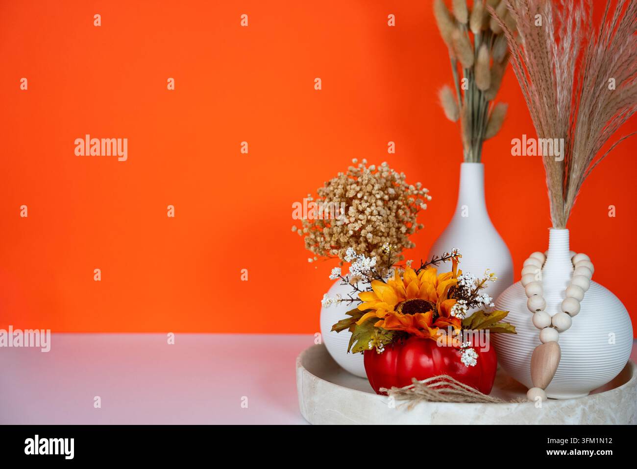 Composizione autunnale accogliente con vasi di ceramica bianchi, piante essiccate, pampa e decorazioni autunnali su uno sfondo rosso intenso. Concetto di estetica degli interni e decorazione per il Ringraziamento. Foto Stock