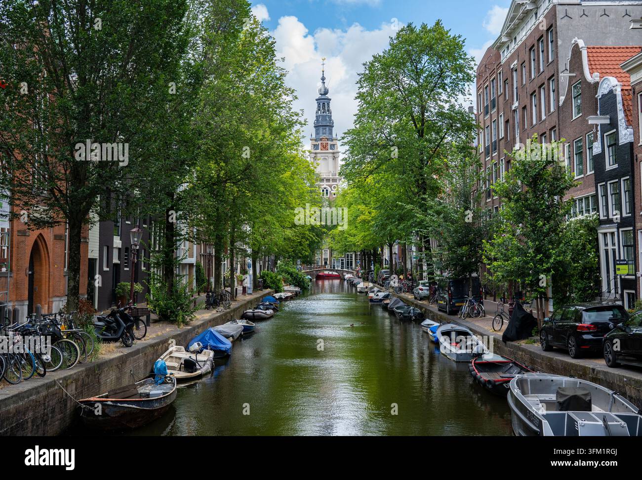 Barche ormeggiate e case sul canale fiancheggiate da alberi lungo la Groenburgwal, con la torre della Zuiderkerk sullo sfondo, Amsterdam, Paesi Bassi. Foto Stock