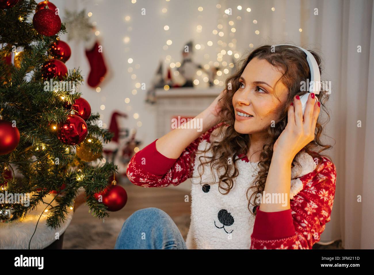 Giovane donna che ascolta la musica natalizia con le cuffie a casa Foto Stock