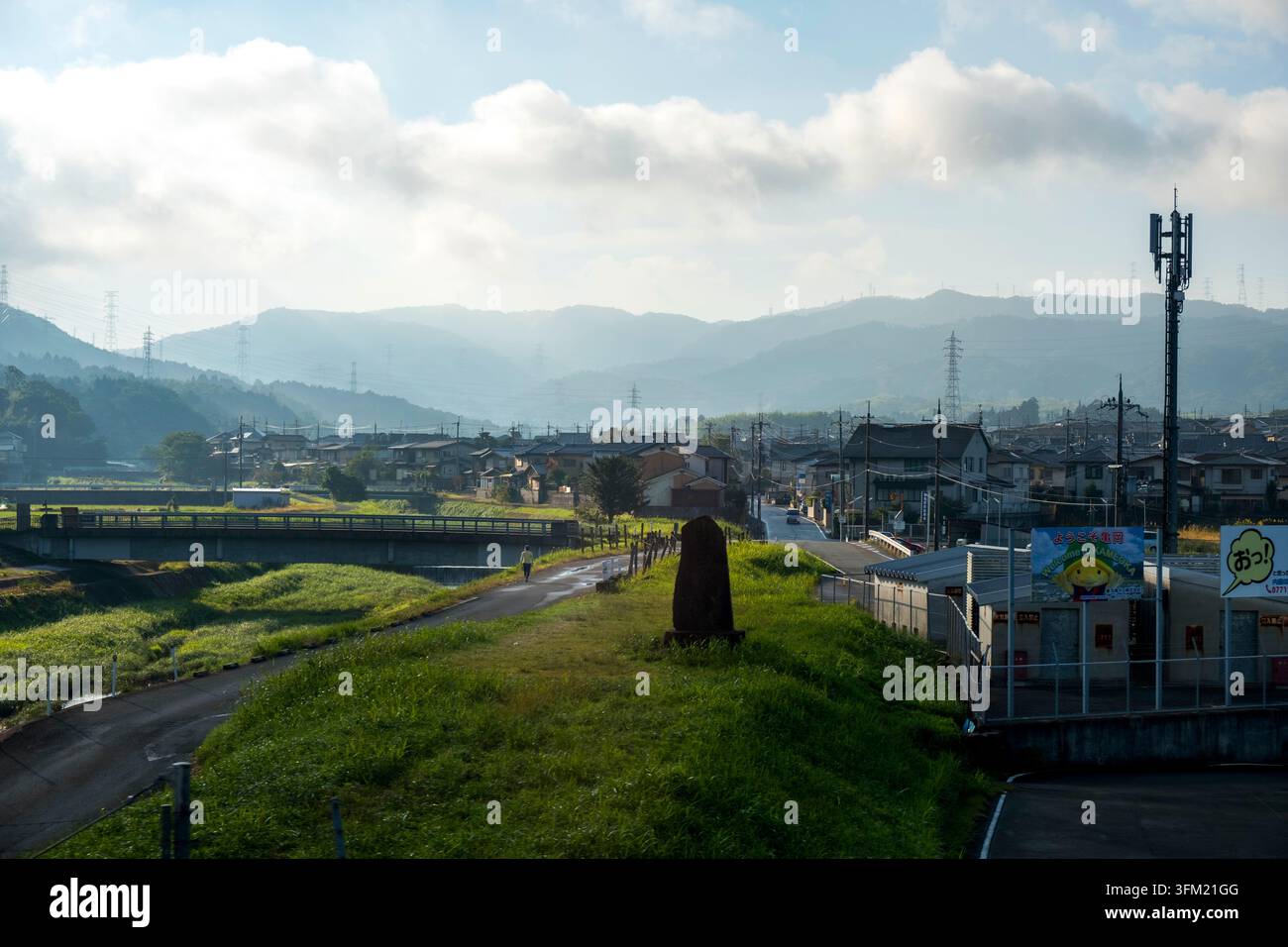 Fiume che scorre attraverso una città rurale giapponese con tralicci ad alta tensione adagiati sulle montagne nella prefettura di Hyogo, Giappone. Foto Stock
